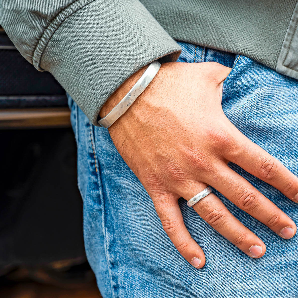 Mans hand hooked on jeans pocket wearing silver cuff and ring
