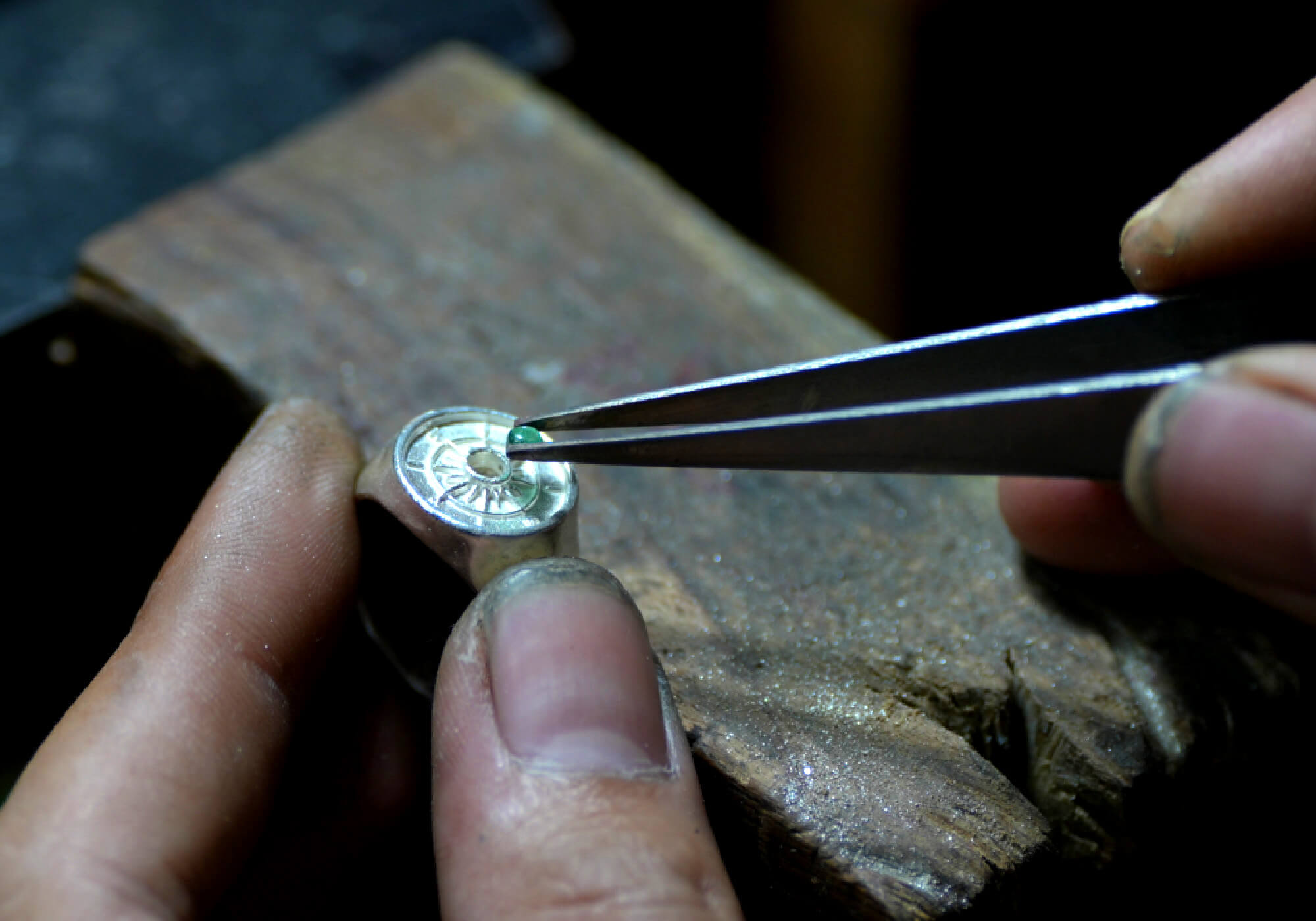 Close-up of a craftsman using tweezers to set an emerald into a ring.