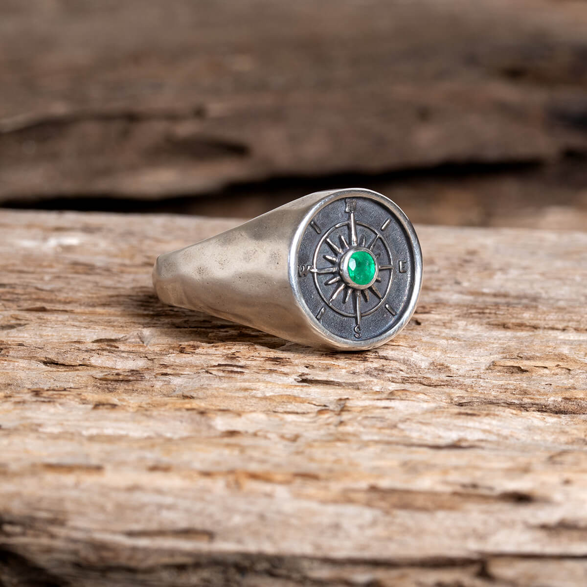 Silver ring with an emerald gemstone on a wooden surface