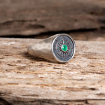 Silver ring with an emerald gemstone on a wooden surface