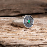 Silver ring with an emerald gemstone on a wooden surface