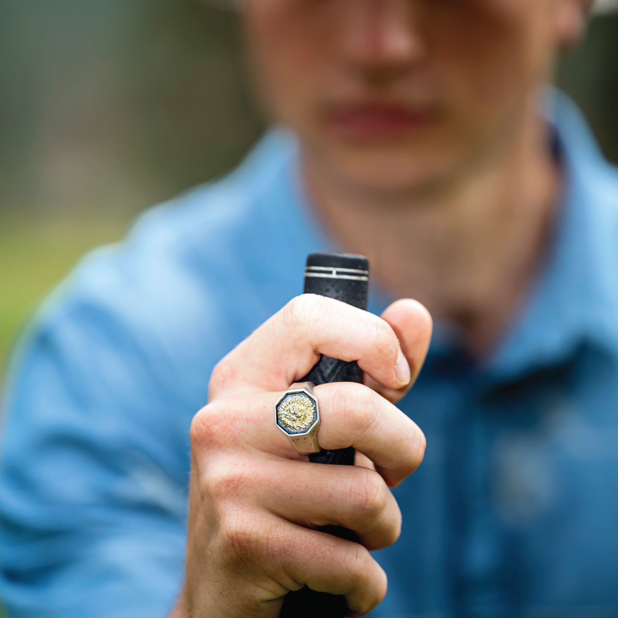 Man holding a golf club wearing silver lion ring.
