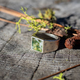 Silver ring with a moss agate stobe on a wooden surface with greenery