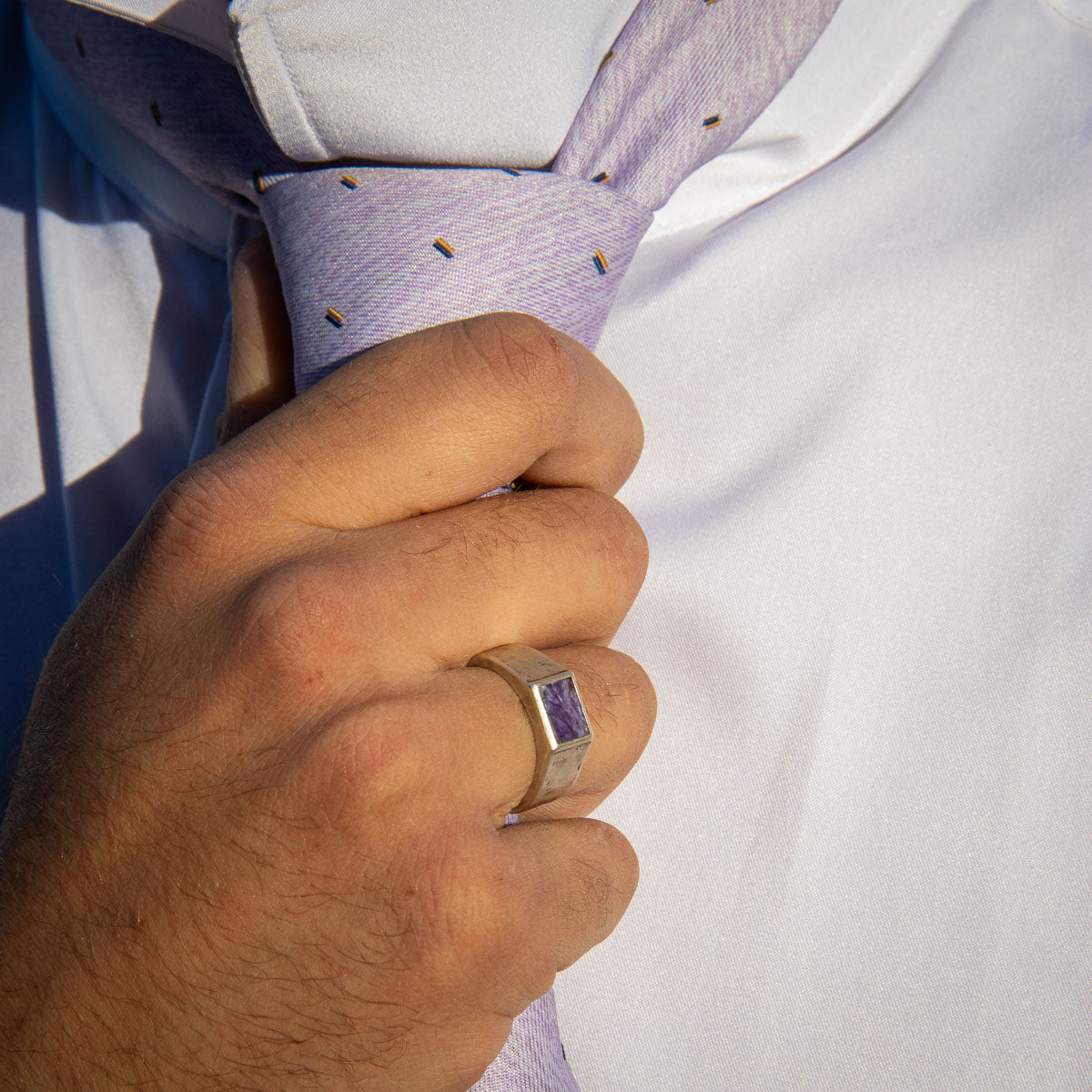 Man straightening necktie wearing lavender and silver signet ring