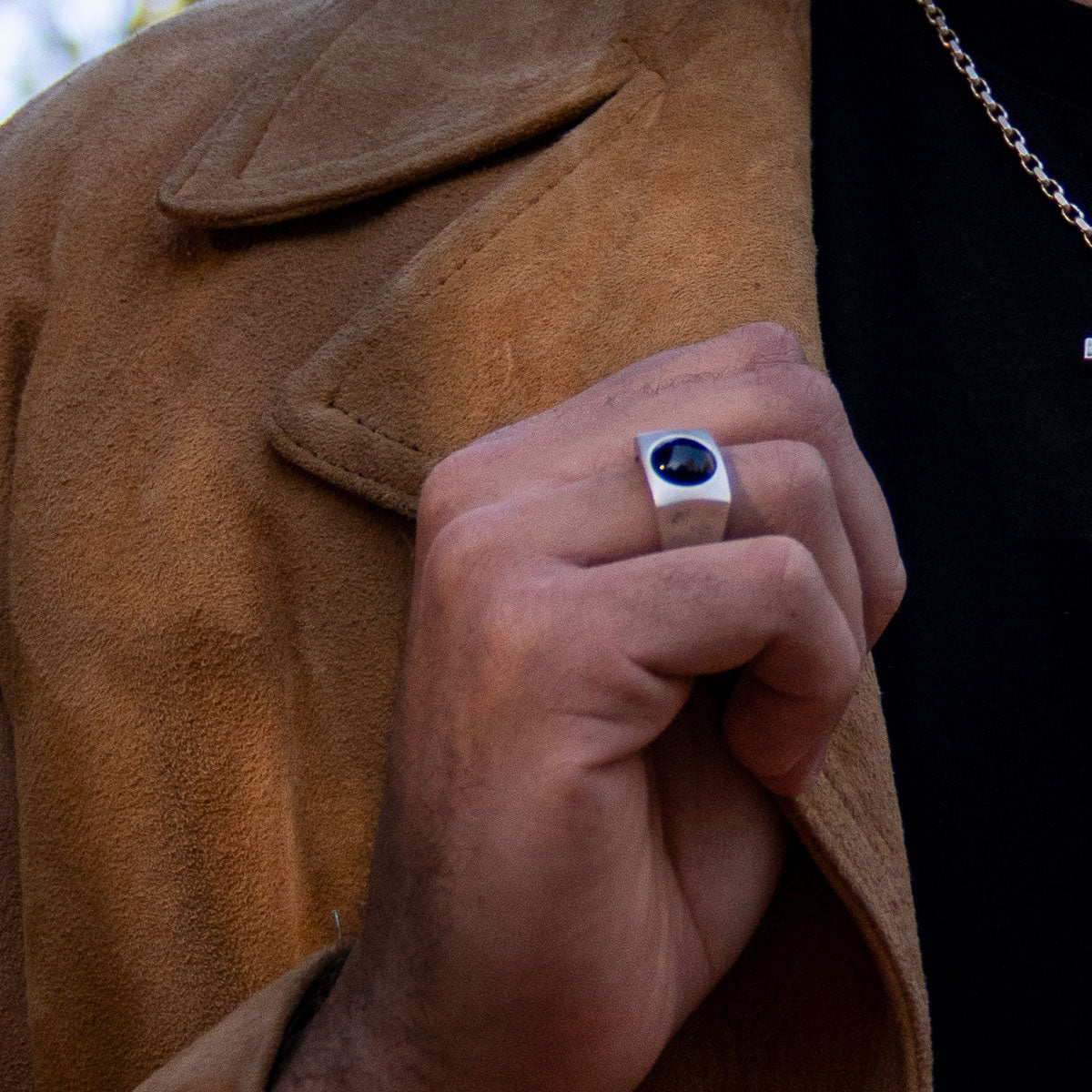 Man holding lapel of suede jacket wearing silver signet ring with onyx cabochon stone