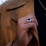 Man holding lapel of suede jacket wearing silver signet ring with onyx cabochon stone