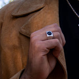 Man holding lapel of suede jacket wearing silver signet ring with onyx cabochon stone