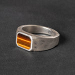 Silver signet ring with a rectangular tiger eye inlay on a dark background
