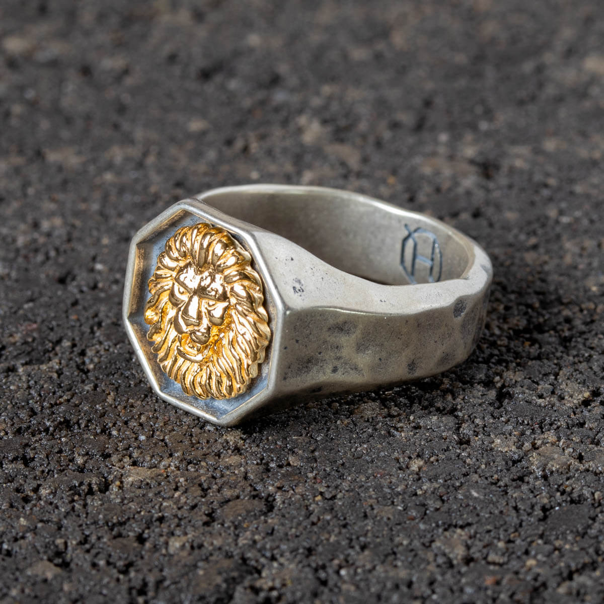 Silver ring with a gold lion emblem on a dark textured surface