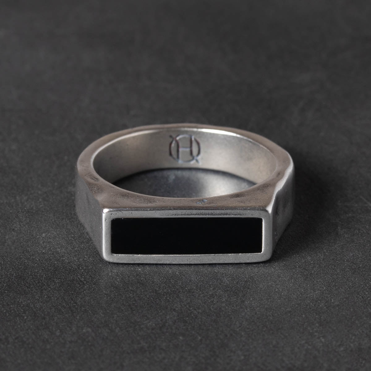 Silver ring with a black rectangular onyx stone on a dark gray background