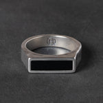 Silver ring with a black rectangular onyx stone on a dark gray background