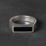 Silver ring with a black rectangular onyx stone on a dark gray background