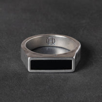 Silver ring with a black rectangular onyx stone on a dark gray background