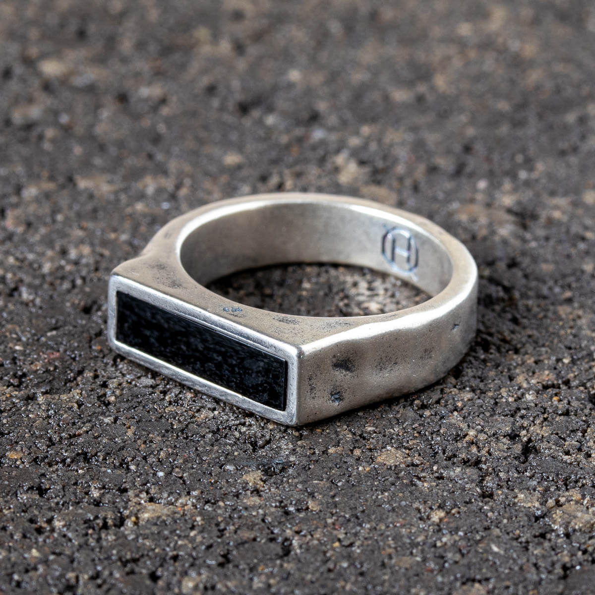 Silver ring with black onyx stone on a dark textured surface