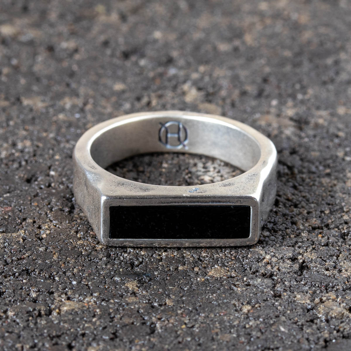 Silver ring with a black onyx stone on a dark textured surface