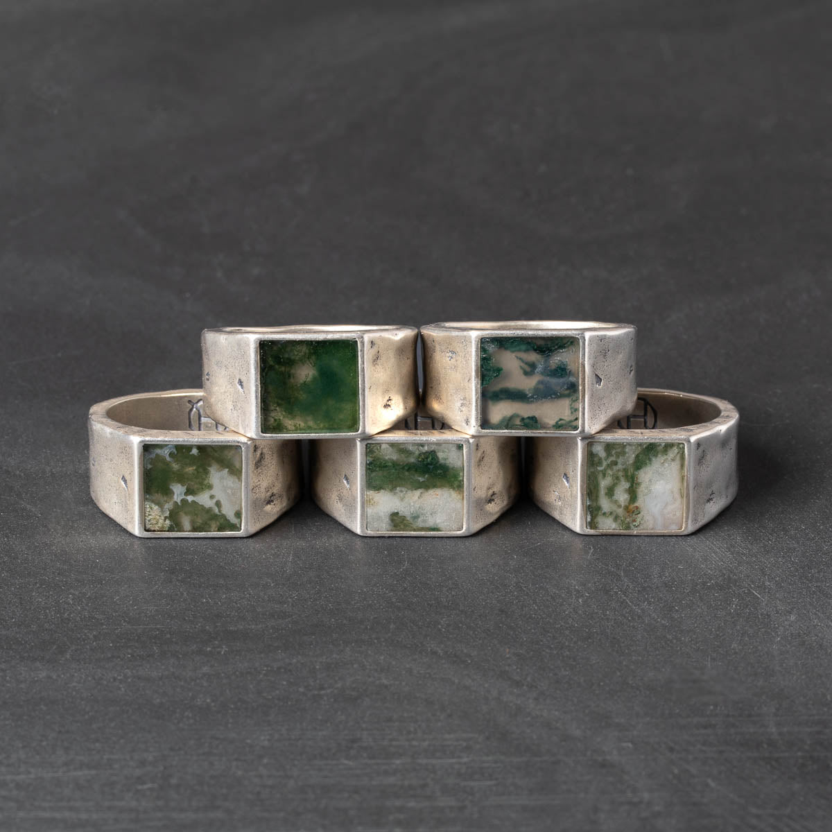 Set of silver rings with square green gemstones on a dark gray background