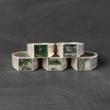 Set of silver rings with square green gemstones on a dark gray background