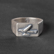 Silver ring with a 1950s hood ornament design on a dark background