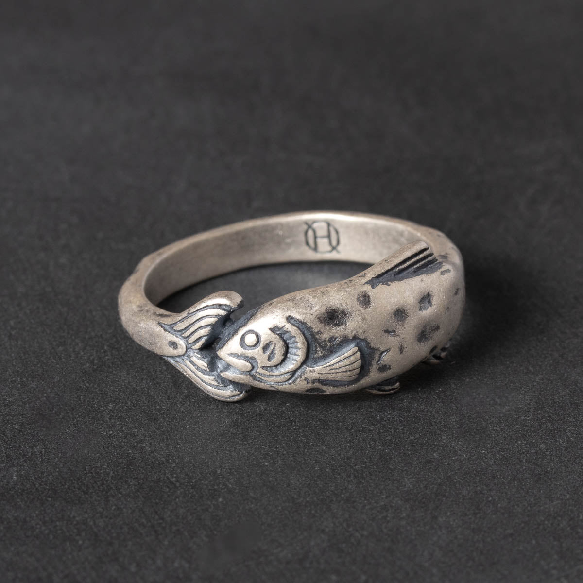 Silver ring with fish design on a dark background