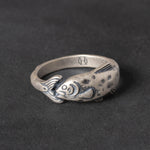 Silver ring with fish design on a dark background