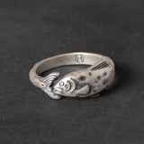 Silver ring with fish design on a dark background