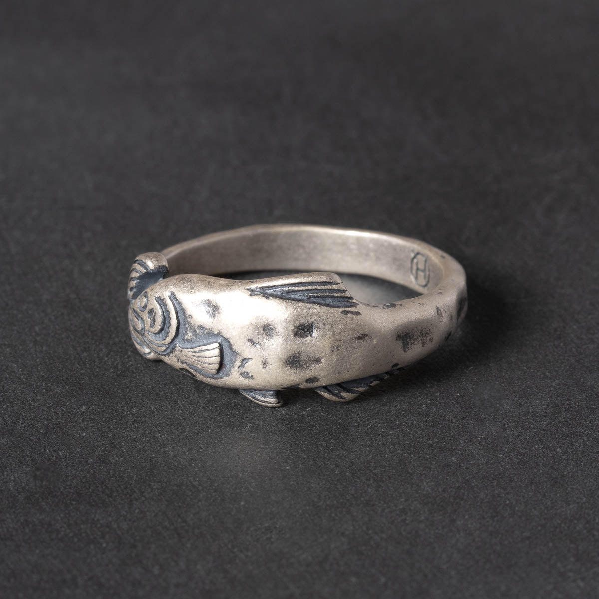 Silver fish-shaped ring on a dark background