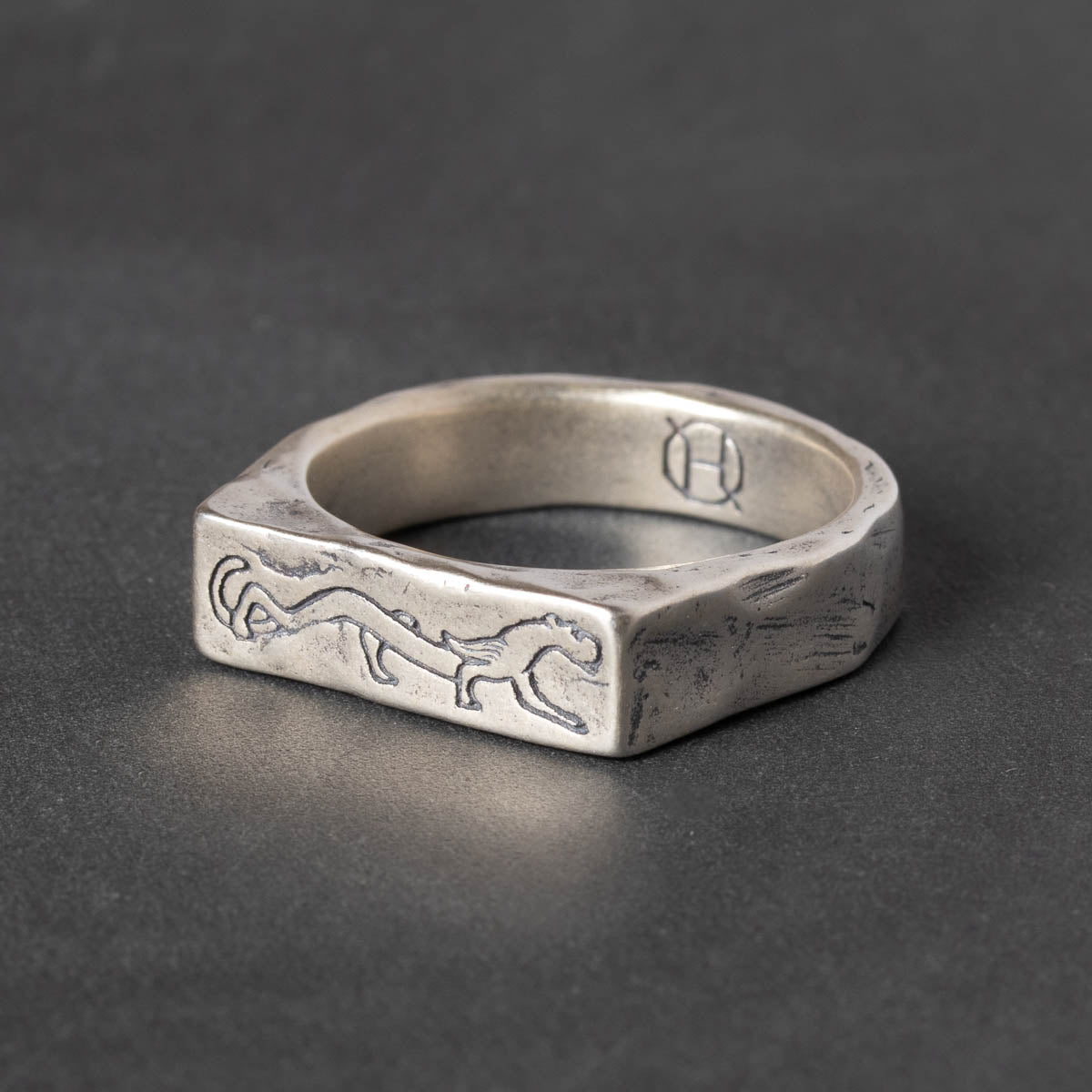 Silver signet ring with engraved stalking panther design on a dark gray background