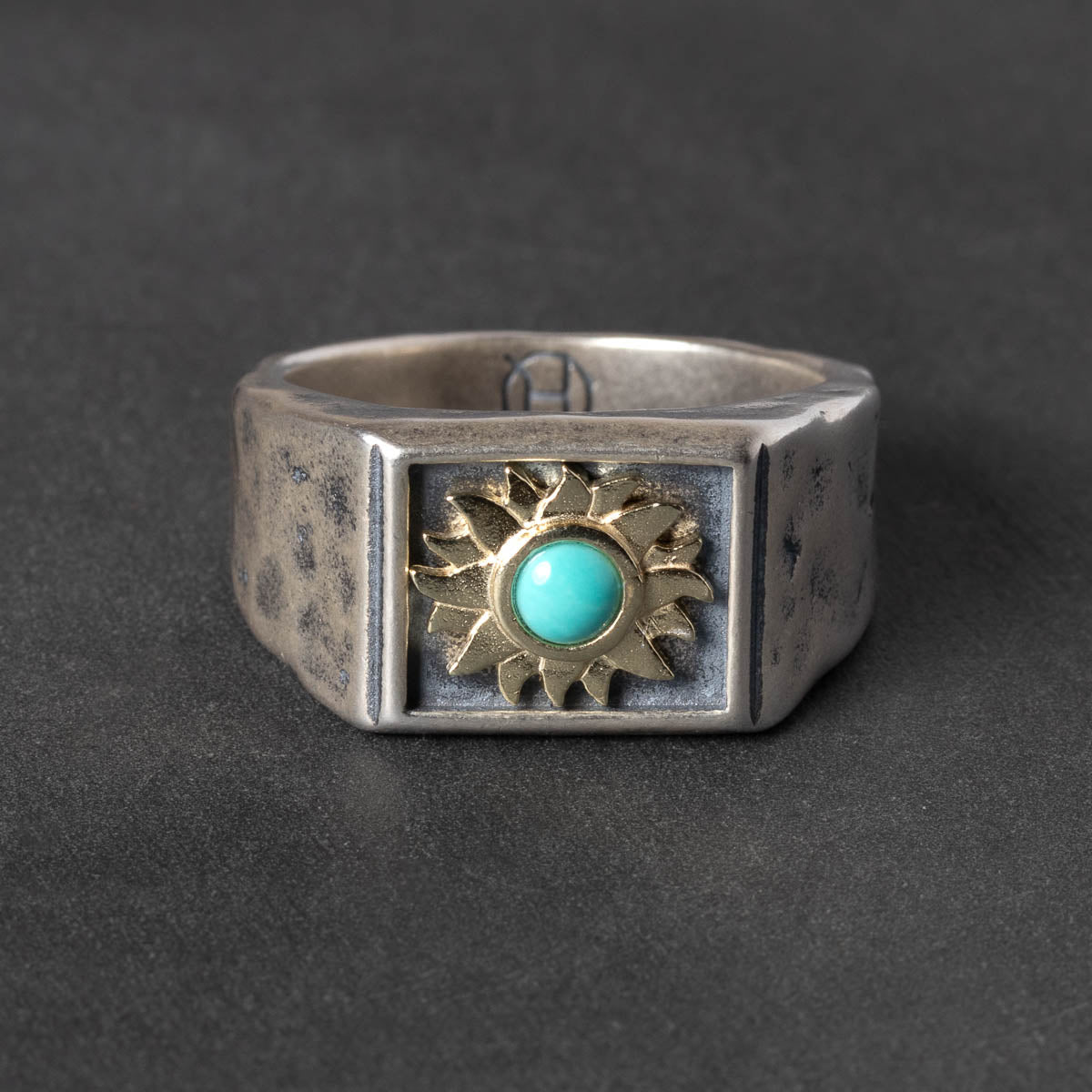 Silver ring with gold sun design and turquoise stone on a dark gray background
