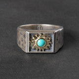 Silver ring with gold sun design and turquoise stone on a dark gray background