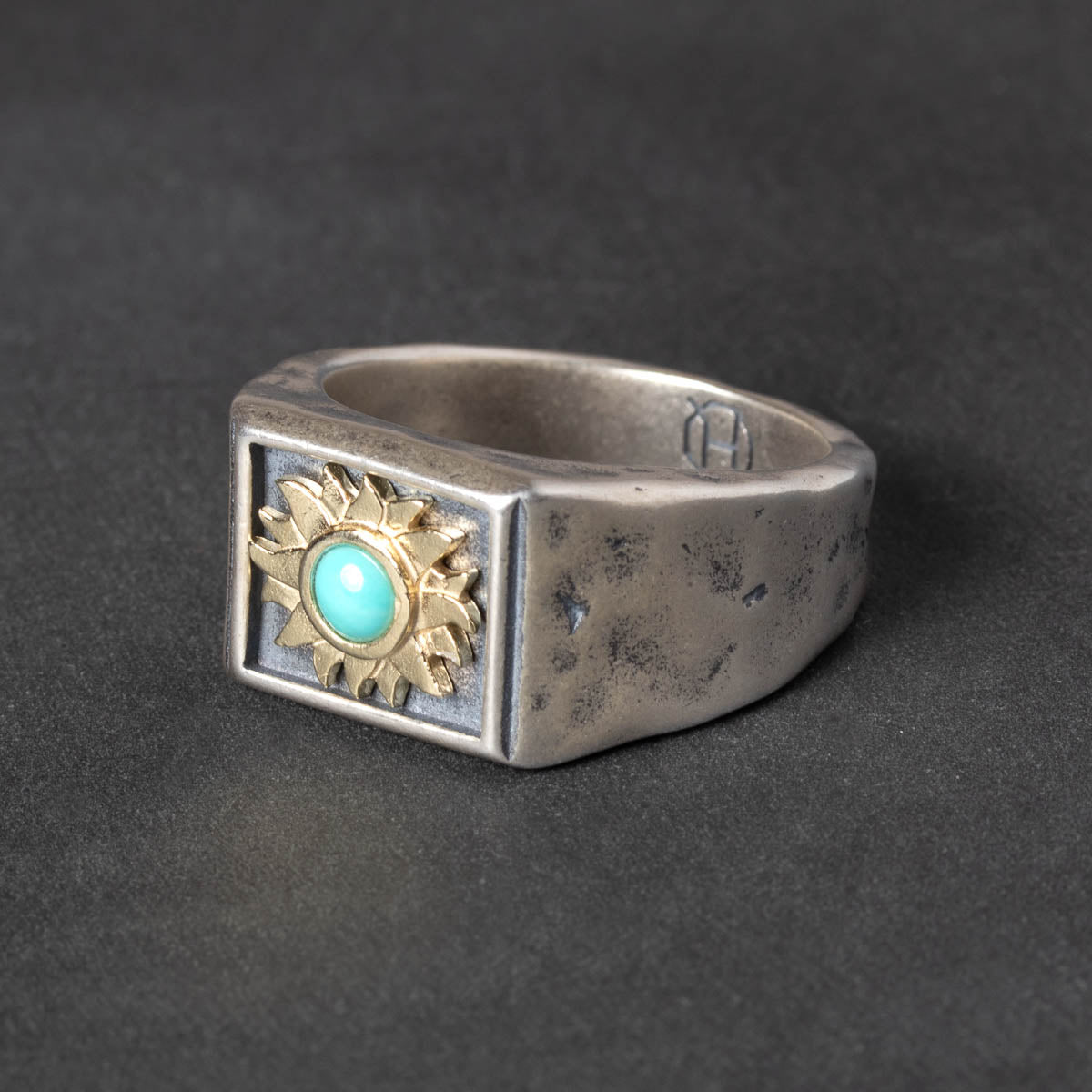 Silver ring with gold sun design and turquoise stone on a dark background