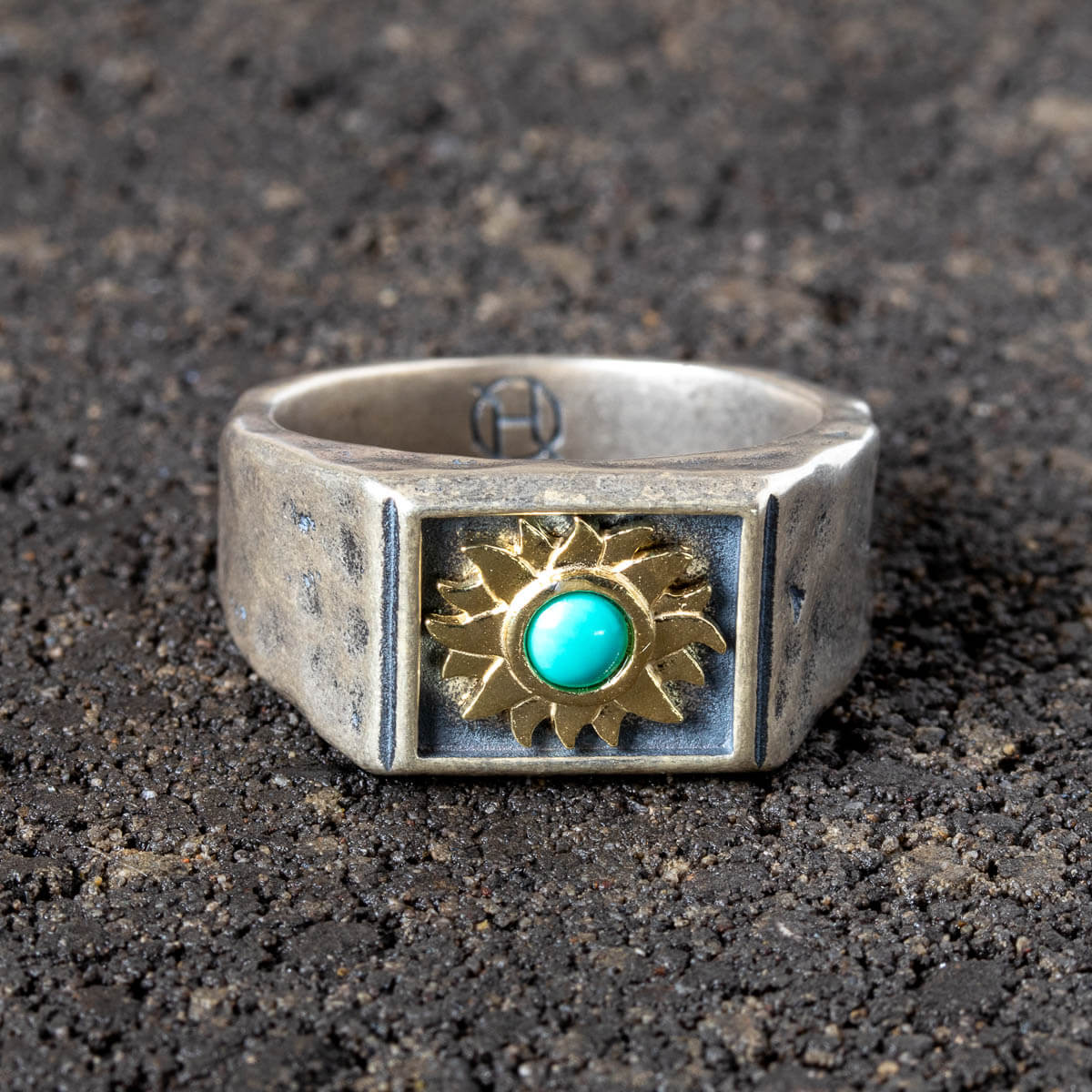 Silver ring with sun design and turquoise stone on a dark textured surface