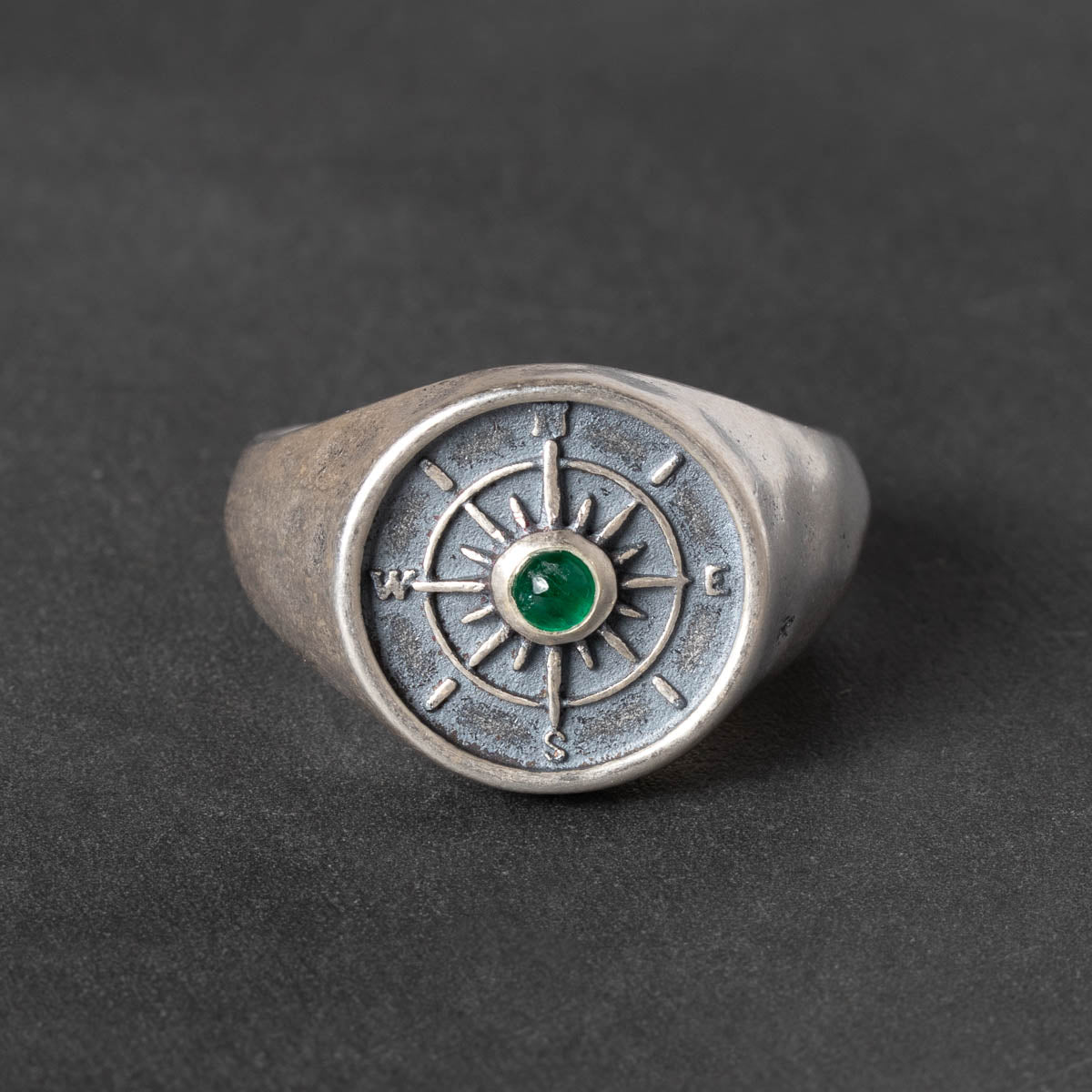 round Silver signet ring with compass design and green emerald cabochon on a dark background