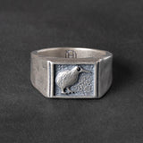 Textured silver signet ring with a kiwi bird carving on a dark background