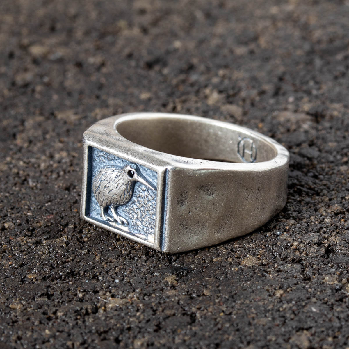Silver ring with a engraved design of a Kiwi on a dark textured surface