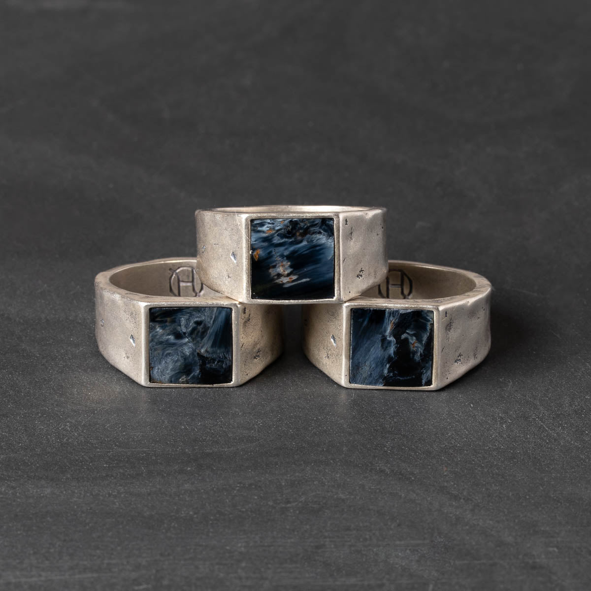 Three silver rings with ilaid pietersite stones on a dark gray background