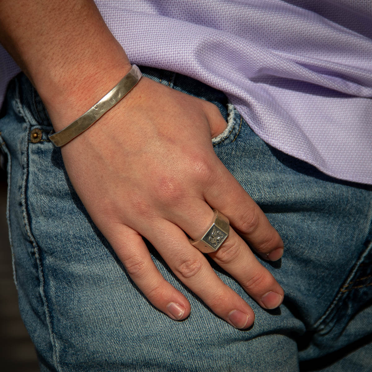Hand with a ring and bracelet, wearing a purple shirt and blue jeans.