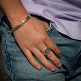 Hand with a ring and bracelet, wearing a purple shirt and blue jeans.