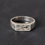 A silver signet ring with engraved frog skeleton on a dark textured background.