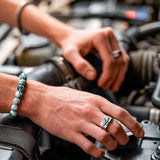 Close-up of hands working on a car engine with a focus on moss agate beaded bracelet.