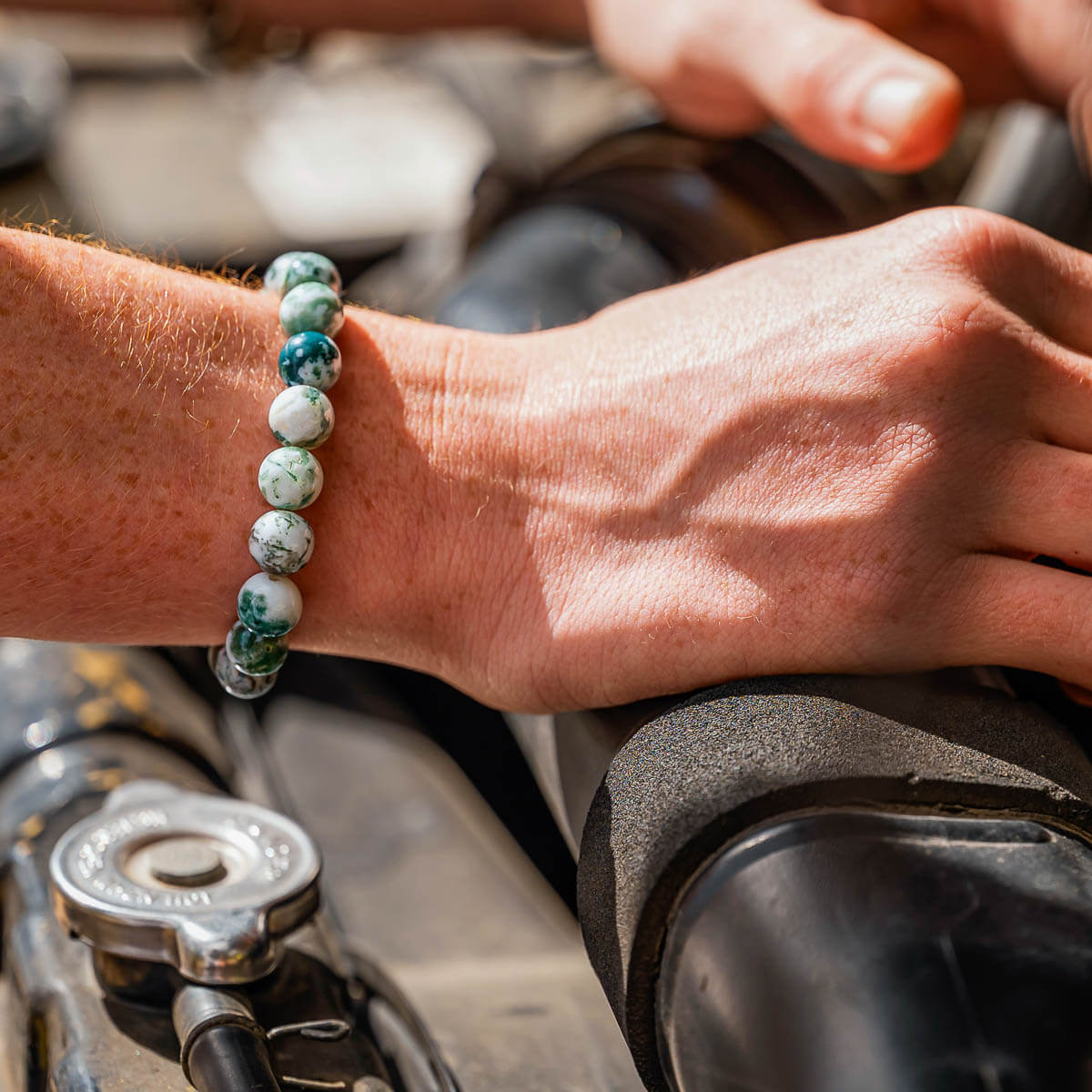 Close-up of a person's wrist wearing a beaded bracelet working on a car