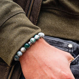 Close-up of a hand wearing a bracelet with green beads, against a background of a jacket and jeans.