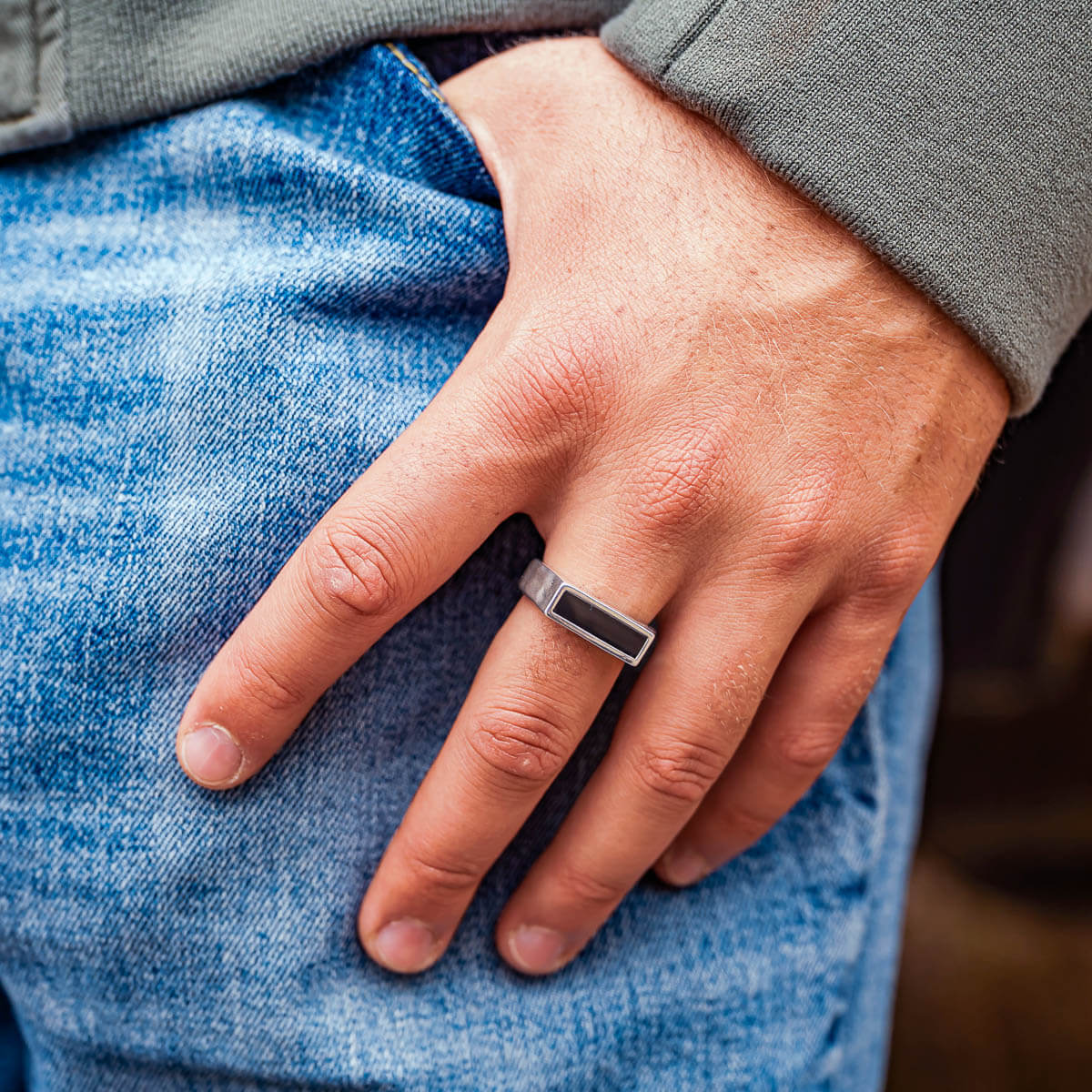 Hand partly in blue jean pocket wearing a silver ring with a black onyx stone