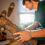 Man holding a large piece of firewood indoors with snowshoes on the wall in the background