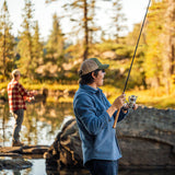 Two people fishing by a lake with trees in the background