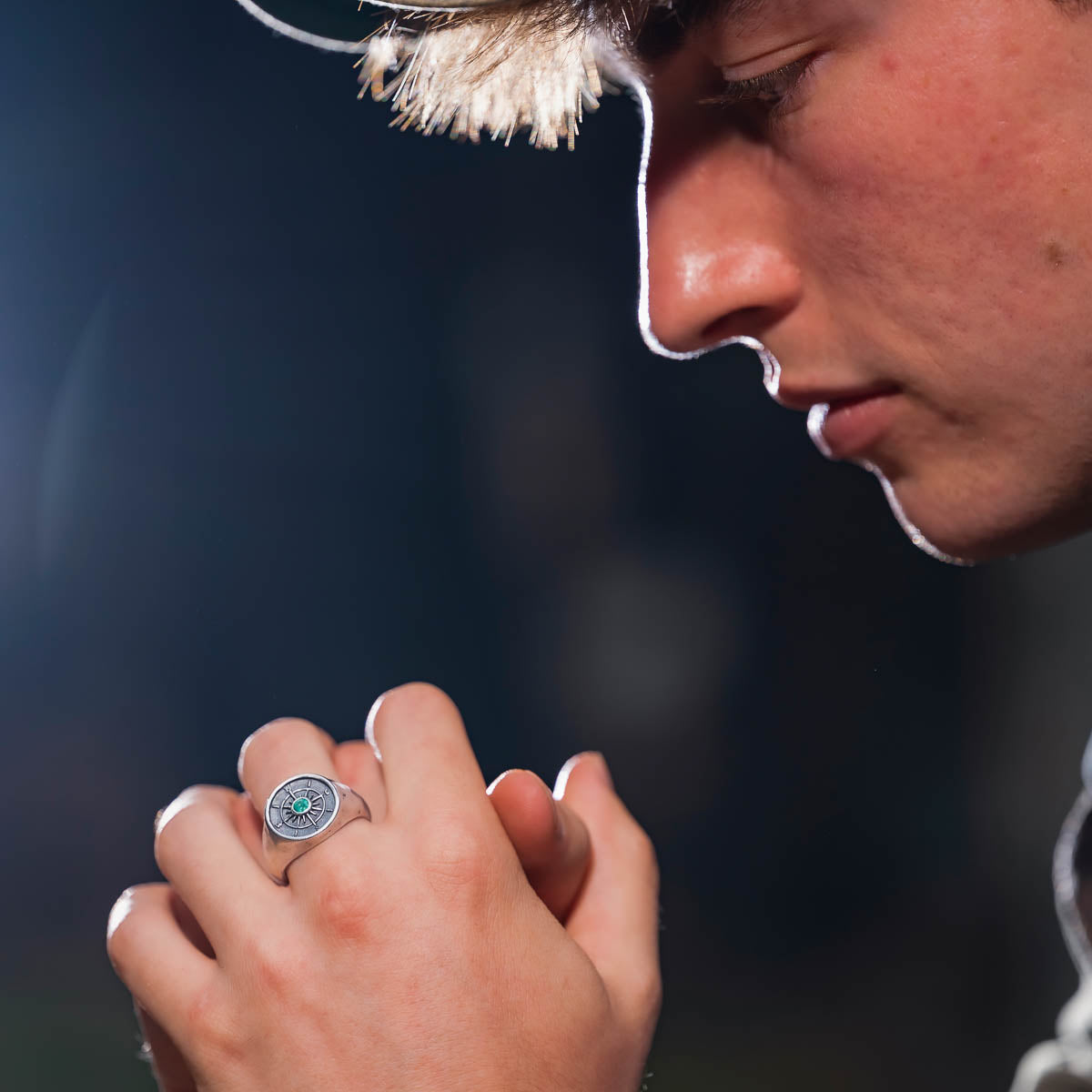 Person wearing a silver compass ring with a dark background