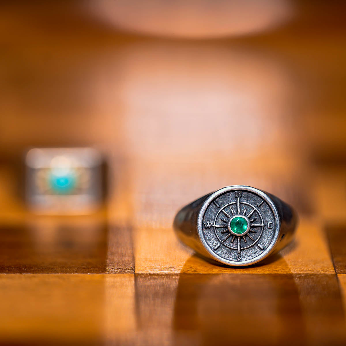 Silver compass ring with an emerald gemstone on a wooden surface