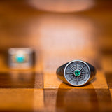 Silver compass ring with an emerald gemstone on a wooden surface