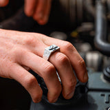 Hand wearing a silver ring with a unique bird design, working on a car engine