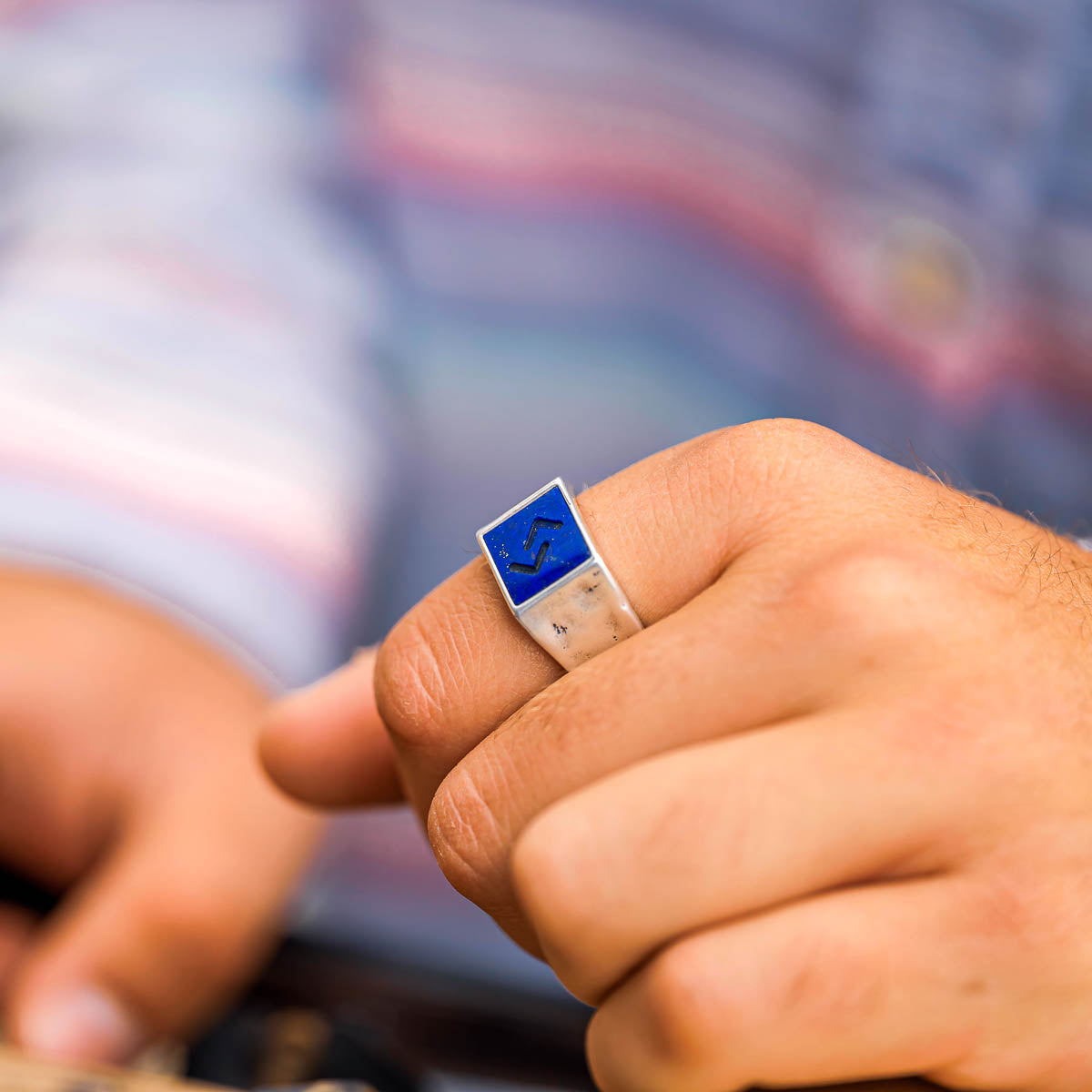 Close-up of a hand wearing a ring with a blue and silver design, blurred background