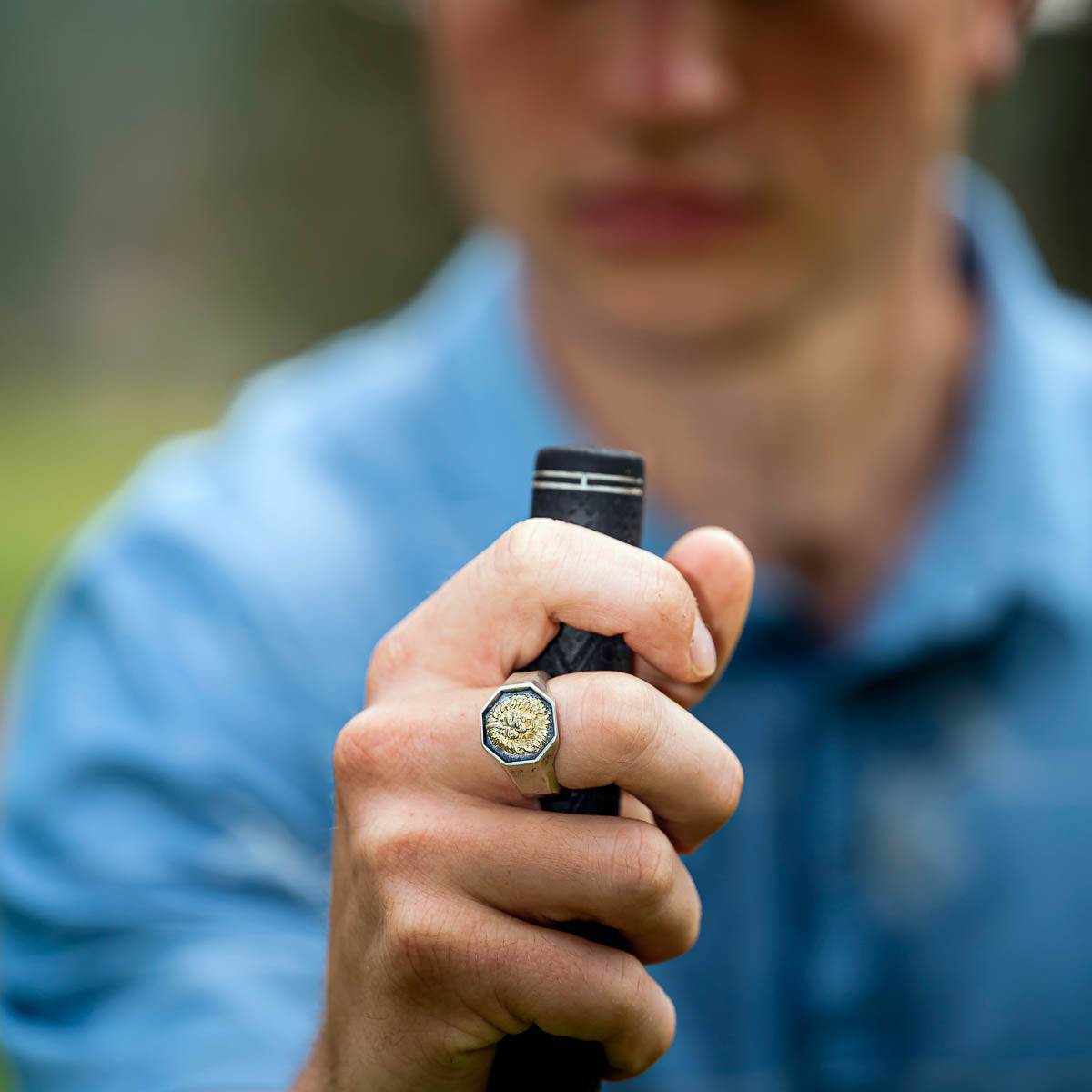 Person wearing a lion signet ring holding a putter grip outdoors